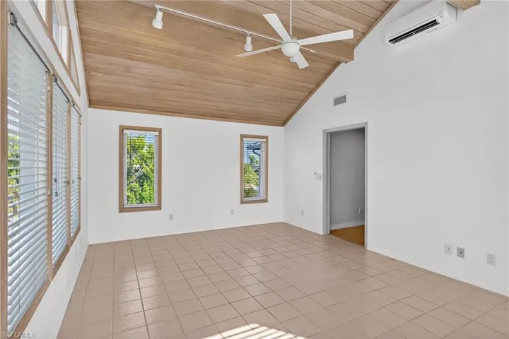 Unfurnished room featuring wooden ceiling, high vaulted ceiling, a wall mounted air conditioner, light tile patterned flooring, and rail lighting