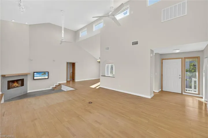 Unfurnished living room featuring ceiling fan, plenty of natural light, a tiled fireplace, and a high ceiling