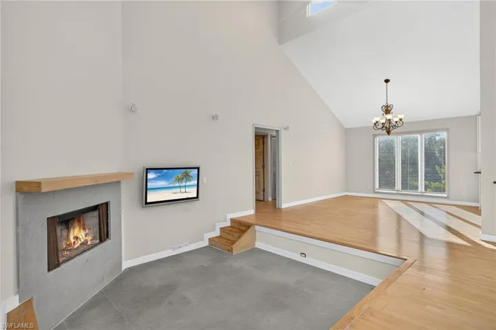 Unfurnished living room featuring high vaulted ceiling, a fireplace, a chandelier, and wood finished floors