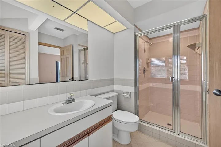 Bathroom featuring a shower stall, vanity, tile walls, light tile patterned floors, and a closet