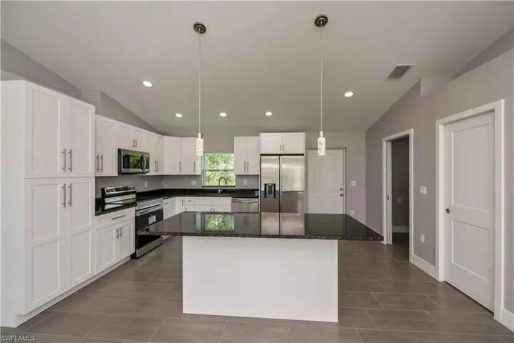 Kitchen with appliances with stainless steel finishes, lofted ceiling, visible vents, and a sink
