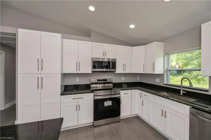 Kitchen featuring vaulted ceiling, stainless steel appliances, a sink, and white cabinetry