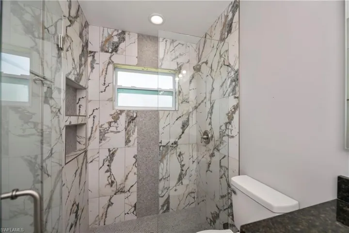 Bathroom with toilet, a marble finish shower, and vanity