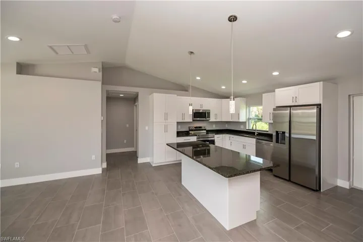 Kitchen featuring stainless steel appliances, vaulted ceiling, white cabinetry, and a sink