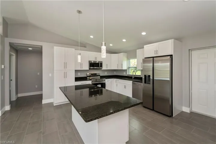Kitchen featuring recessed lighting, stainless steel appliances, a kitchen island, white cabinetry, and vaulted ceiling