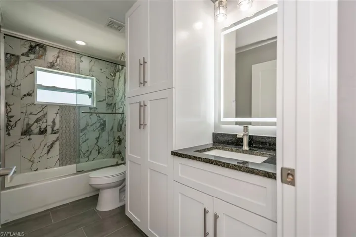 Full bathroom with toilet, enclosed tub / shower combo, visible vents, and vanity