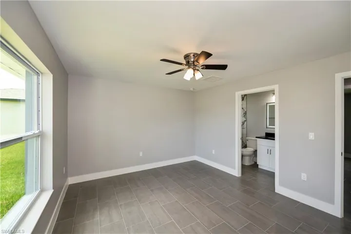 Unfurnished bedroom with ceiling fan, multiple windows, baseboards, and ensuite bathroom