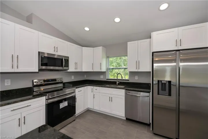 Kitchen featuring white cabinets, dark stone counters, vaulted ceiling, stainless steel appliances, and a sink
