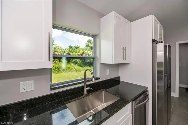 Kitchen with dark stone counters, appliances with stainless steel finishes, a sink, and white cabinets