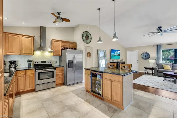 Kitchen featuring ceiling fan, stainless steel appliances, wine cooler, wood finish cabinetry, and vaulted ceiling