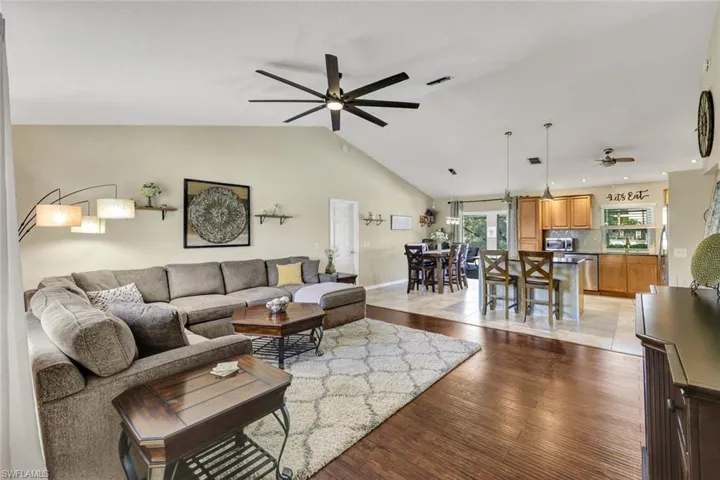Living area with dark wood-style flooring, a ceiling fan, and vaulted ceiling