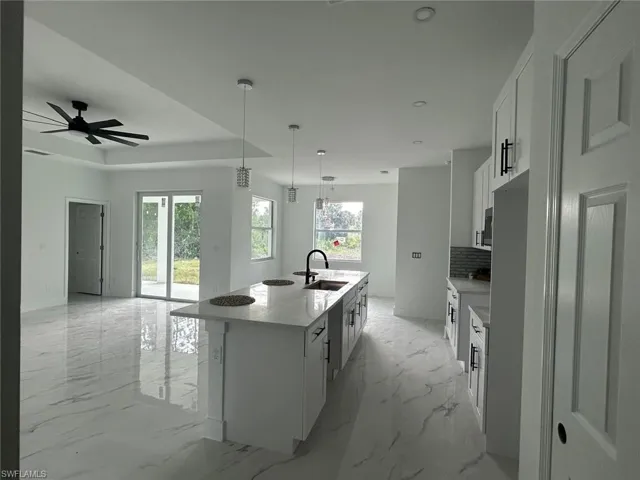 Kitchen featuring healthy amount of natural light, tasteful backsplash, white cabinetry, a large island with sink, and recessed lighting