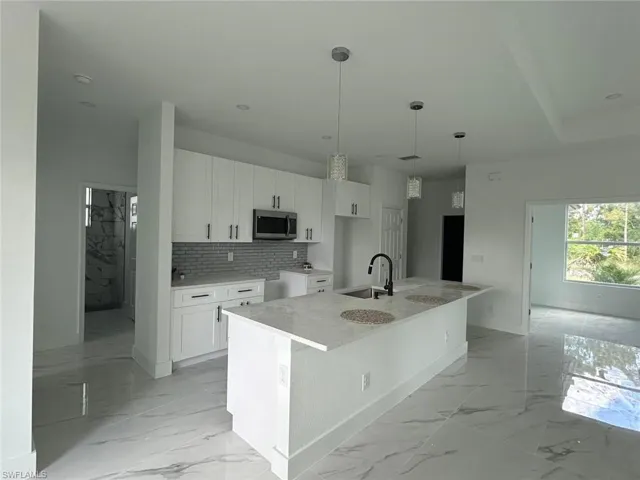 Kitchen featuring stainless steel microwave, light marble finish floors, white cabinetry, backsplash, and recessed lighting