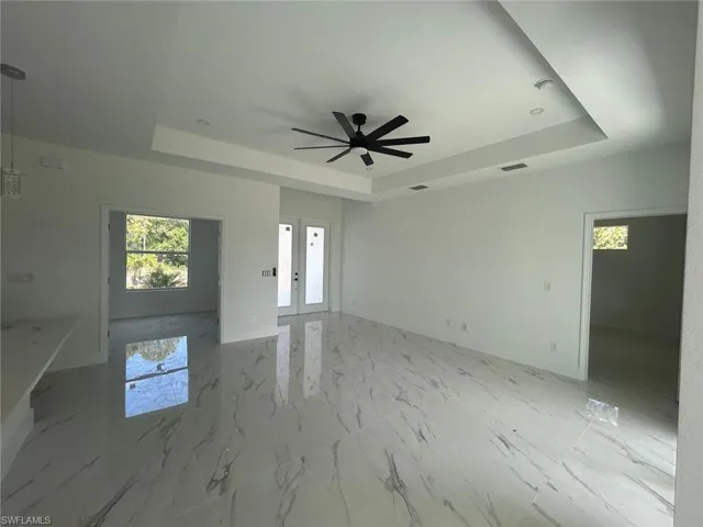 Unfurnished living room featuring a raised ceiling, a ceiling fan, french doors, and light marble finish flooring