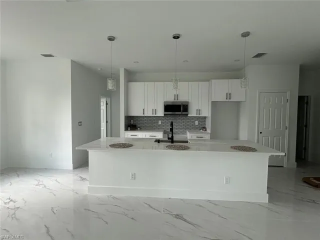 Kitchen with stainless steel microwave, a large island, white cabinets, and light marble finish flooring
