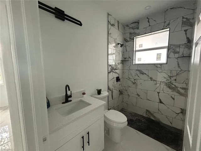 Full bath featuring a tile shower, vanity, and marble look tile flooring