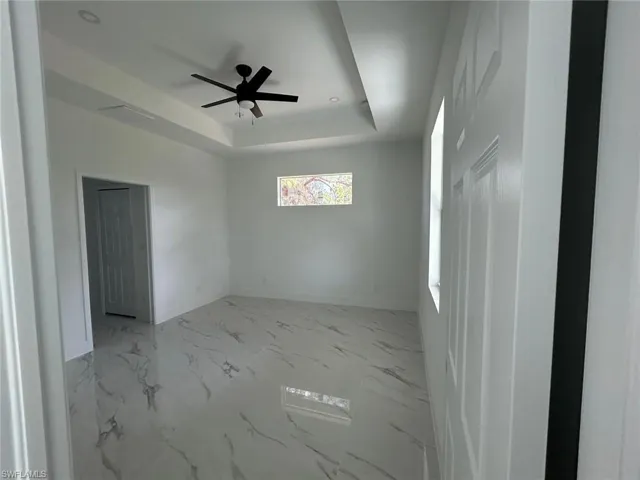 Unfurnished room with ceiling fan, a tray ceiling, and marble finish floors