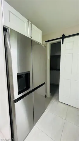 Kitchen with stainless steel refrigerator with ice dispenser, white cabinetry, light tile patterned floors, and a barn door