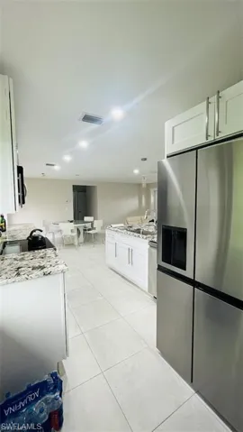Kitchen with stainless steel fridge with ice dispenser, a peninsula, white cabinetry, light tile patterned floors, and light stone counters
