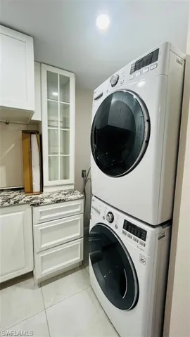 Laundry area with stacked washer / drying machine, light tile patterned flooring, and cabinet space