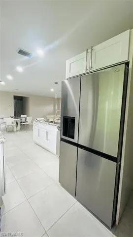 Kitchen with stainless steel fridge, white cabinetry, and light tile patterned floors
