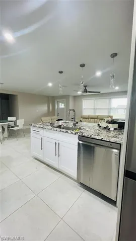 Kitchen with dishwasher, ceiling fan, light stone counters, and white cabinets