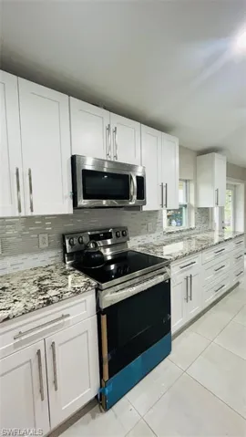 Kitchen with appliances with stainless steel finishes, white cabinetry, and decorative backsplash