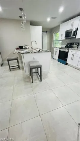 Kitchen with stainless steel appliances, decorative backsplash, a barn door, white cabinetry, and light tile patterned floors