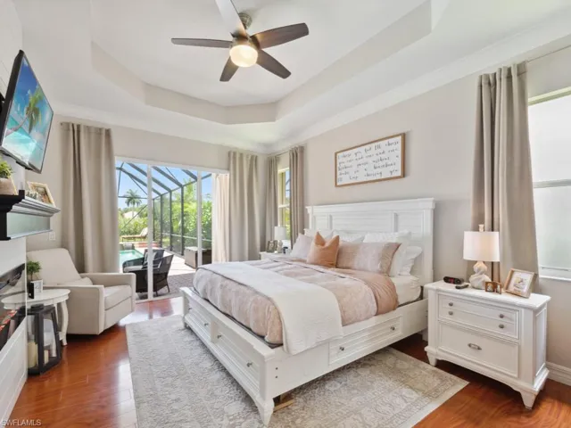 Bedroom featuring wood-type flooring, a tray ceiling, access to exterior, and ceiling fan
