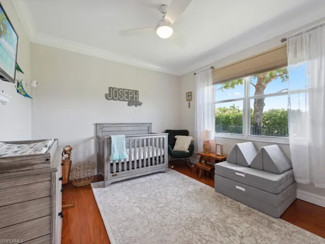 Bedroom featuring a crib, crown molding, dark hardwood / wood-style floors, and ceiling fan