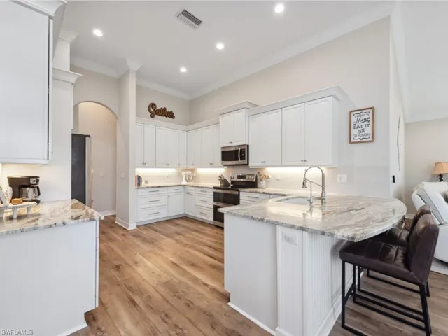 Kitchen featuring crown molding, sink, light stone countertops, light hardwood / wood-style floors, and appliances with stainless steel finishes