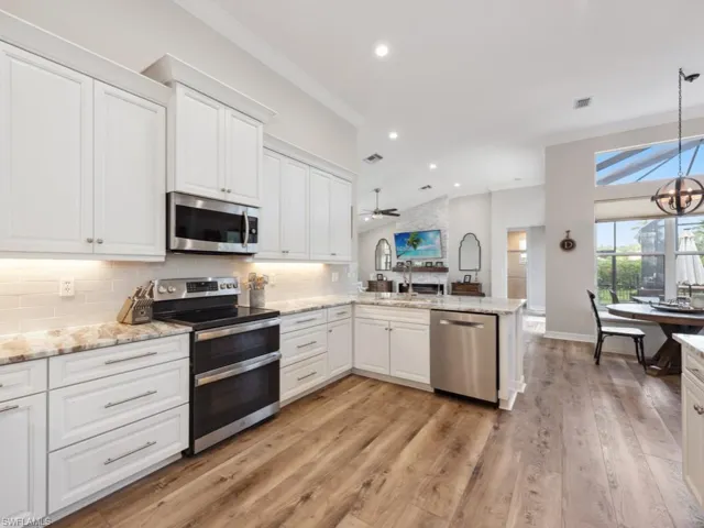 Kitchen with light hardwood / wood-style flooring, stainless steel appliances, white cabinets, kitchen peninsula, and decorative backsplash