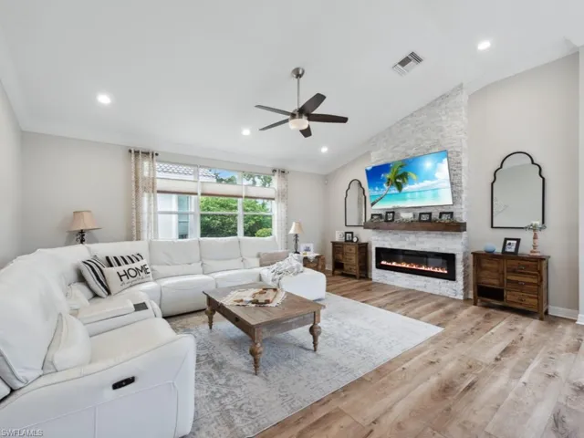 Living room with a fireplace, crown molding, light wood-type flooring, lofted ceiling, and ceiling fan