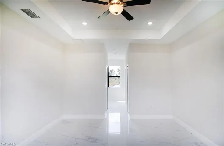 Tiled empty room with a tray ceiling and ceiling fan