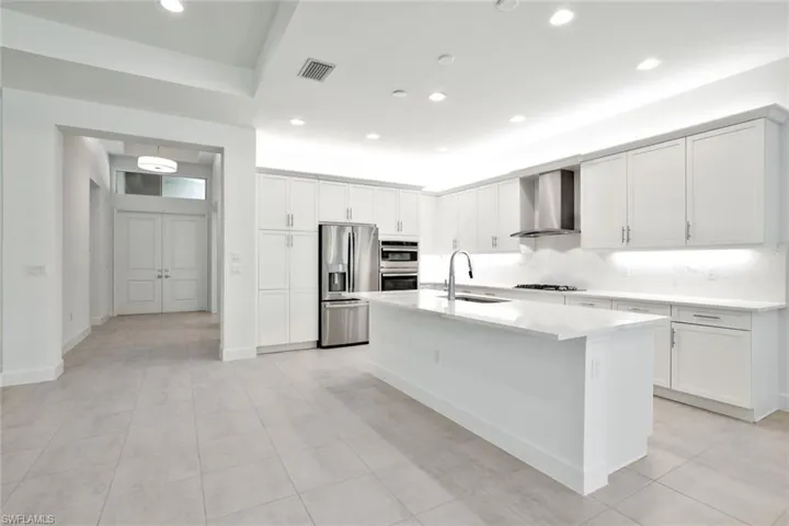 Kitchen with appliances with stainless steel finishes, an island with sink, wall chimney exhaust hood, and light tile floors