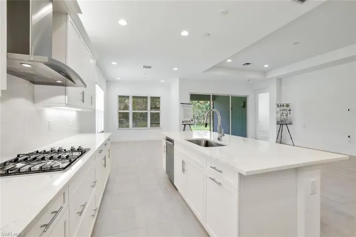 Kitchen with wall chimney range hood, a center island with sink, and light tile floors