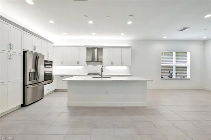 Kitchen with stainless steel appliances, wall chimney range hood, sink, and light tile floors