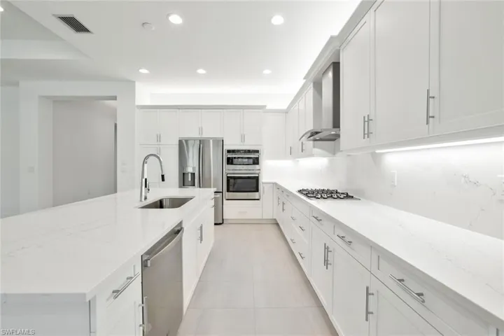 Kitchen featuring stainless steel appliances, light tile flooring, wall chimney range hood, sink, and white cabinetry