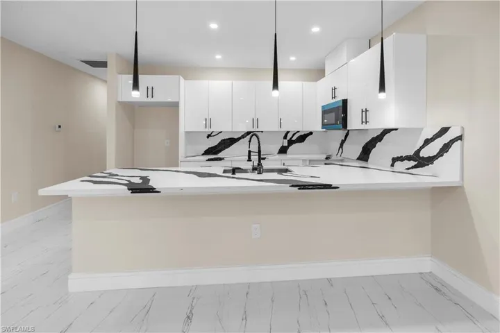 Kitchen featuring a peninsula, pendant lighting, white cabinets, light stone counters, and a breakfast bar area