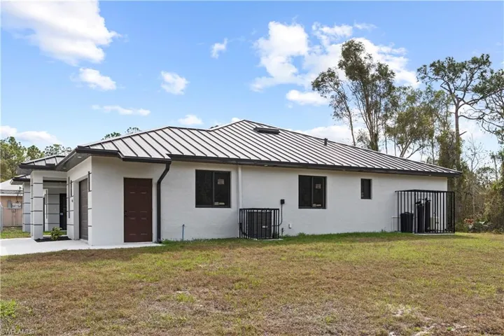 Back of house with stucco siding, a yard, and a standing seam roof