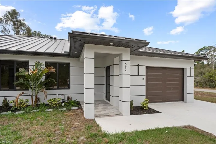 Modern home featuring a standing seam roof, an attached garage, stucco siding, and driveway