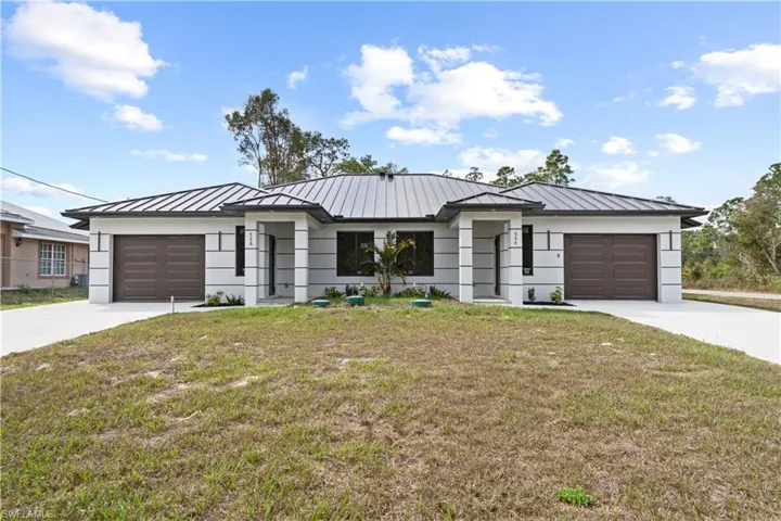 View of front of home with a front lawn, an attached garage, driveway, and a standing seam roof