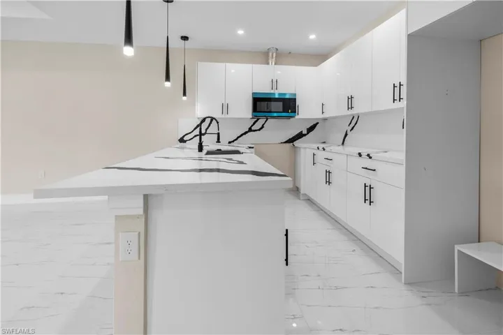 Kitchen with white cabinetry, stainless steel microwave, pendant lighting, light stone counters, and light marble finish floors
