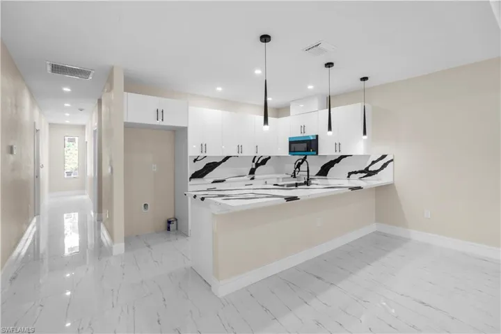 Kitchen with a peninsula, light marble finish floors, stainless steel microwave, pendant lighting, and white cabinets