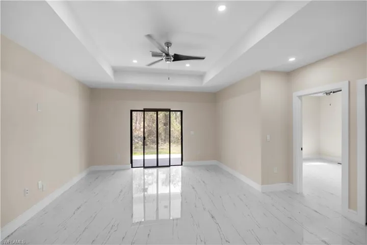 Empty room with a ceiling fan, light marble finish floors, recessed lighting, and a tray ceiling