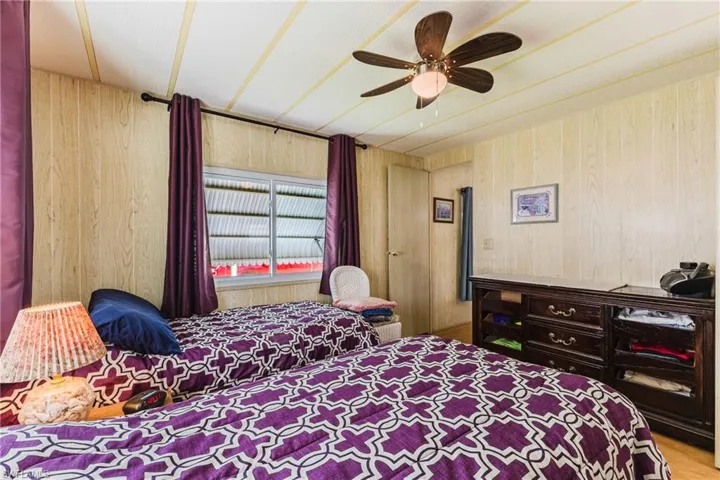 Wood-paneled walls with a window, dark wood-finish dresser, and ceiling fan with integrated lighting