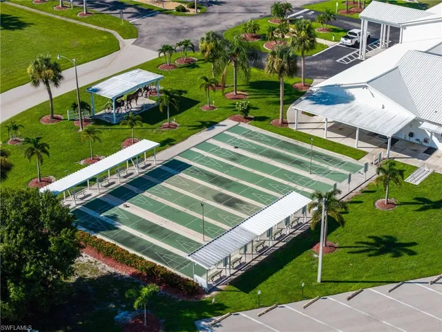 Multiple shuffleboard courts with covered seating areas, surrounded by manicured lawns and mature palm trees