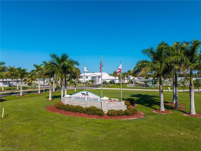 Manicured green lawn with a "Carriage Village" entrance sign and palm trees