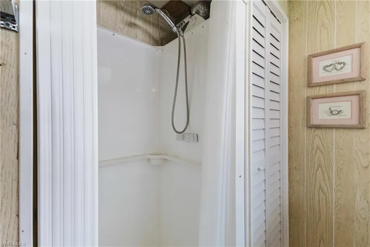 White shower stall with a flexible shower head and a bi-fold louvered door