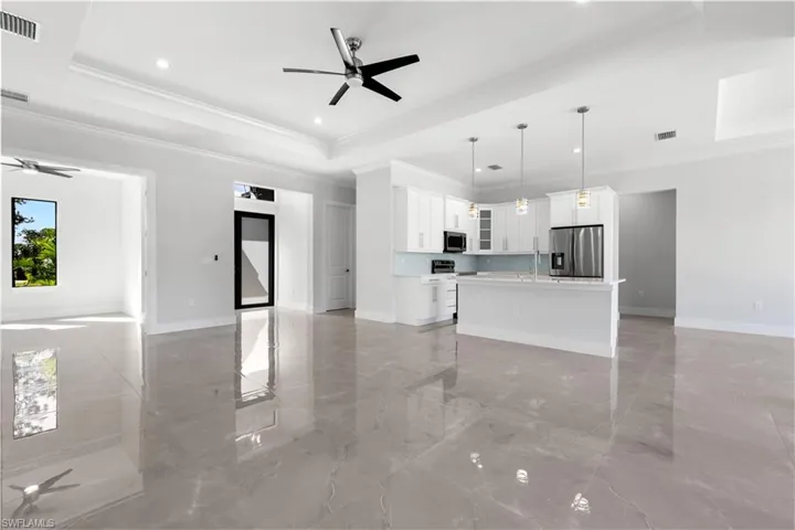 Unfurnished living room featuring ceiling fan, a tray ceiling, light marble finish floors, crown molding, and recessed lighting